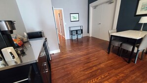 A kitchen with a microwave, coffee maker, and a sink. There is a dining table with chairs and a small cabinet. The floor is wooden, and there is a door leading to another room. - The Loft on Winter - Downtown Adrian (Adrian)