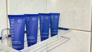 A bathroom with a shelf holding four Thalassa shampoo and conditioner bottles.