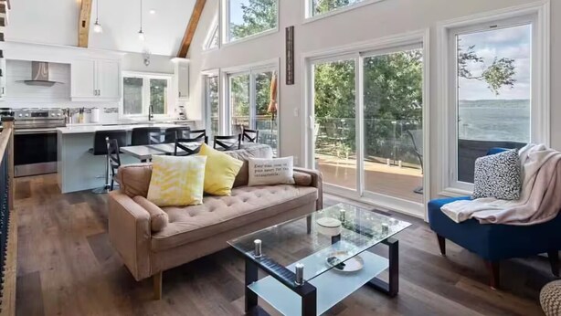 A spacious living area with a large glass table, a sofa with cushions, and a view of the outdoors through large windows.