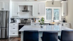 A modern kitchen with white cabinets, stainless steel appliances, a large island with bar stools, and a window providing natural light.