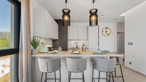 Une cuisine moderne dotée d’un îlot central, de tabourets de bar, de luminaires suspendus et offrant une vue sur l’extérieur grâce à une grande fenêtre.
