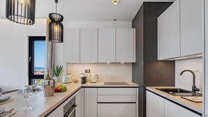 Une cuisine moderne avec des meubles blancs, un plan de travail en bois, un évier et des luminaires suspendus.