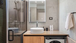 Une salle de bain moderne avec un lavabo rond, un grand miroir, un lave-linge encastré et un porte-serviettes.