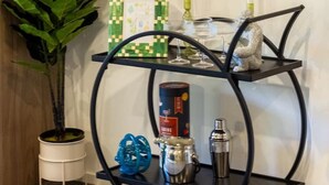 Une étagère en métal noir, sur laquelle sont posés un tableau encadré de vert et de blanc, une plante en pot et une bouteille d’huile d’olive.
