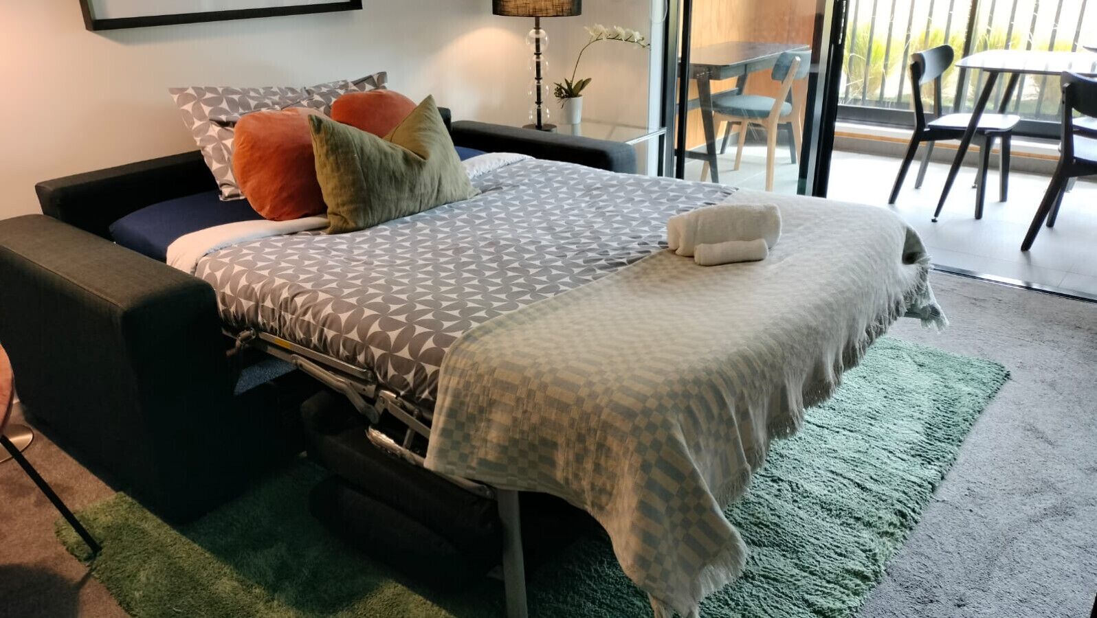 A modern bedroom with a bed, a green rug, and a view of the outside.