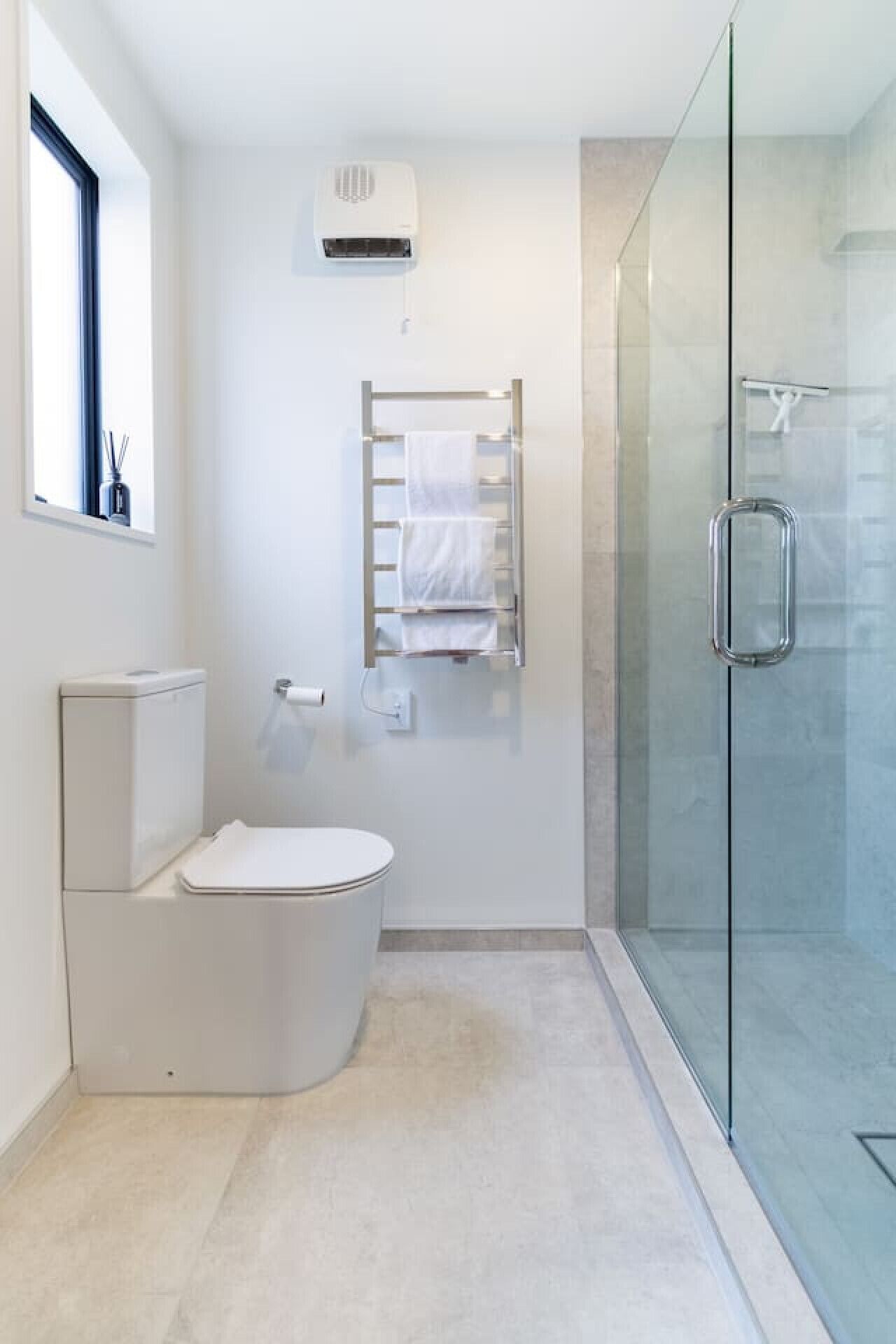 Un baño moderno con inodoro, cabina de ducha de vidrio y un perchero para toallas.