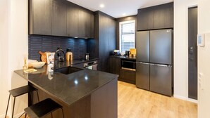 Une cuisine moderne avec des meubles de couleur sombre, un îlot central doté de tabourets, un four encastré et un réfrigérateur en acier inoxydable.