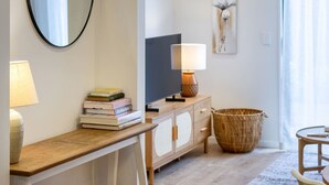 Un salon moderne avec un bureau en bois, des livres, une lampe, un téléviseur, un panier en osier et un tableau accroché au mur.