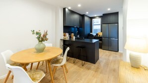 Une cuisine moderne avec des meubles de couleur sombre, un îlot central et un coin repas comprenant une table ronde en bois et des chaises blanches.
