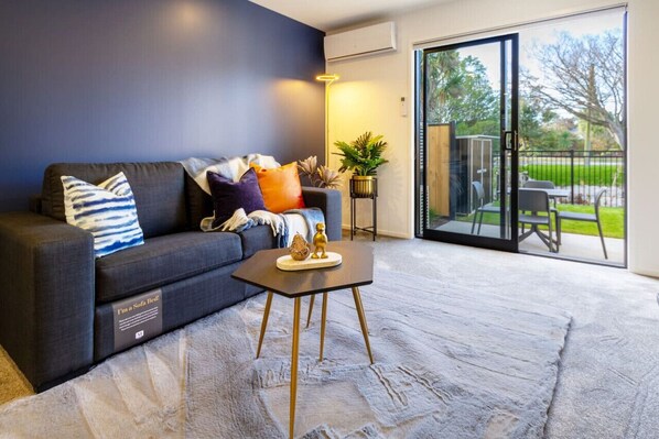 Una sala de estar moderna con una pared azul oscuro, un sofá gris con almohadones decorativos, una mesita redonda con base dorada y una alfombra gris grande.