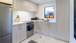 A modern kitchen with light wood cabinets, a stainless steel refrigerator, a built-in oven, and a window providing a view of the outside.