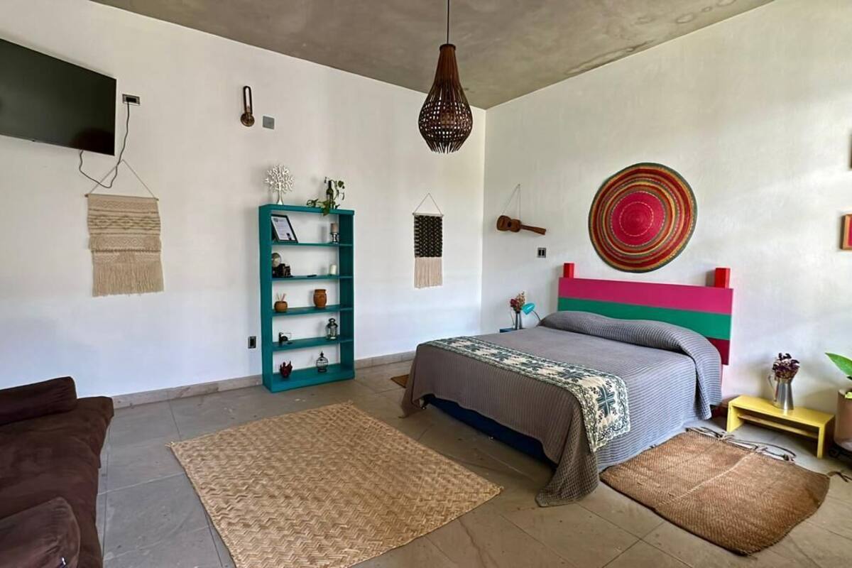 A bedroom with a bed, a TV, a bookshelf, and a wall-mounted guitar.