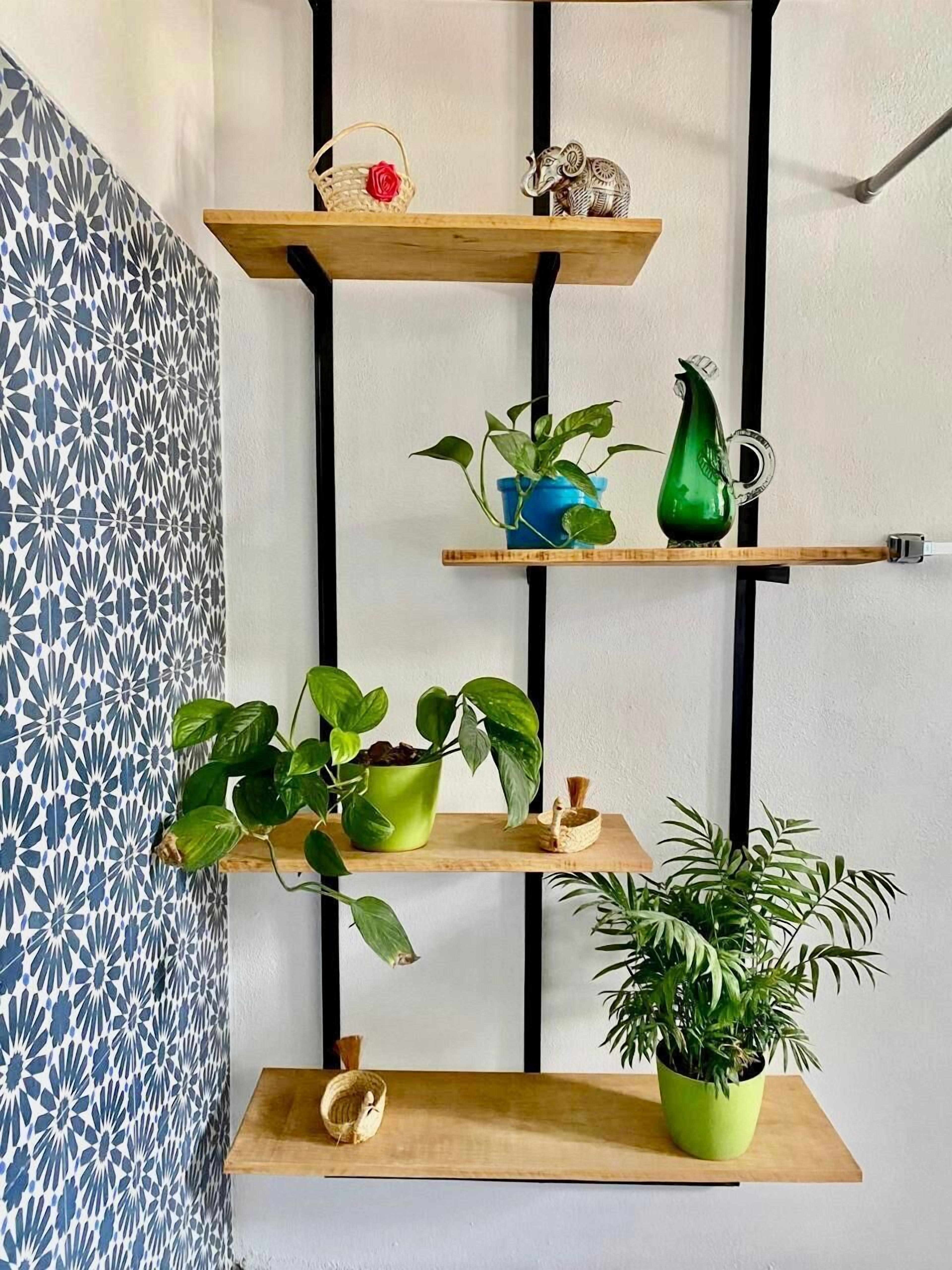 A wall-mounted shelf with three tiers, each holding various decorative items and plants.