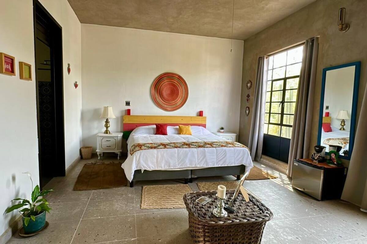 A bedroom with a bed, bedside tables, a wicker basket, and a window with curtains.