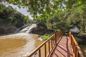 A wooden bridge over a river with a waterfall, surrounded by lush greenery. - Pousada Cachoeira da Barra (Cunha)