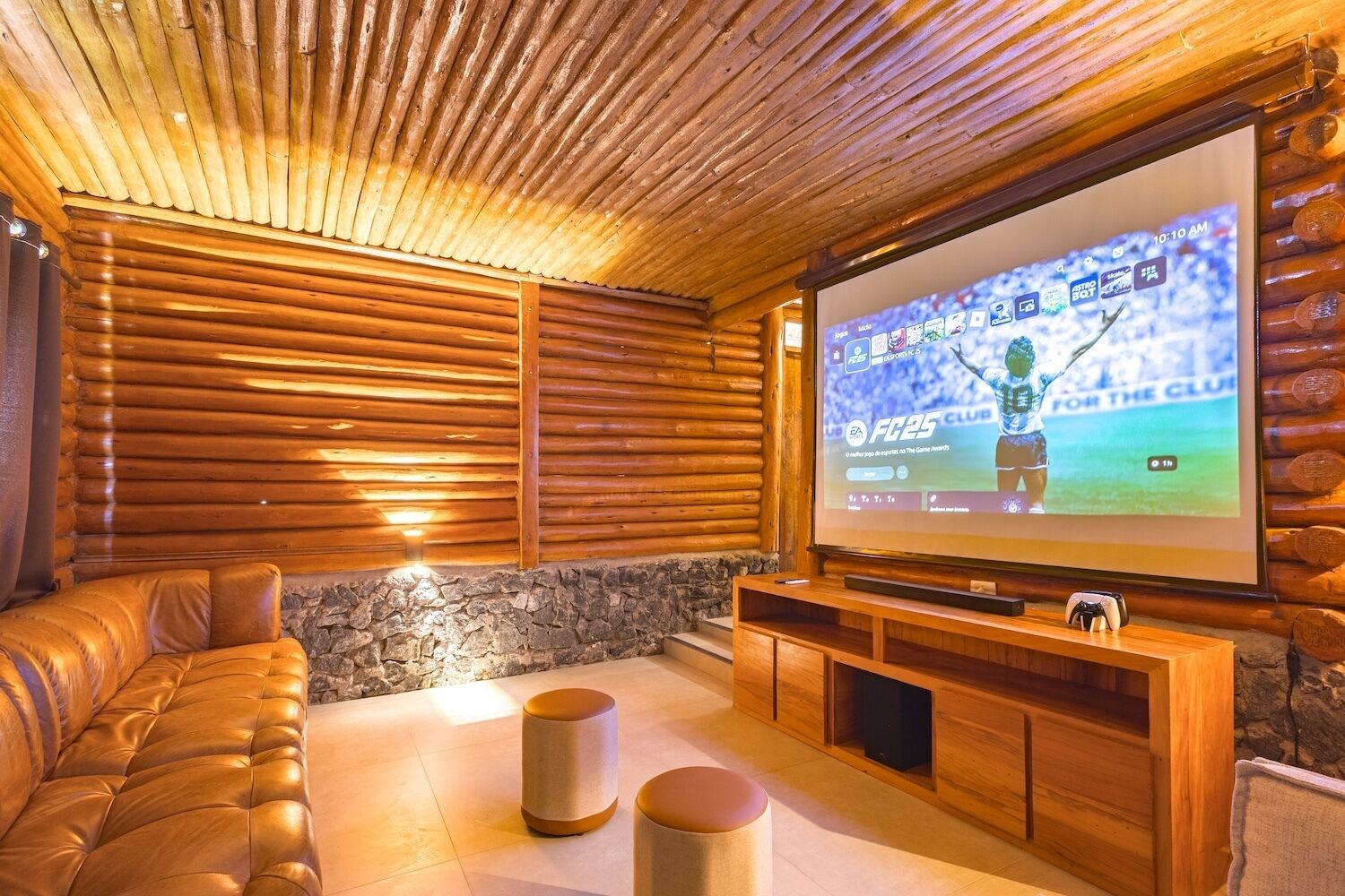 Ein gemütliches Blockhaus-Interieur mit einem großen Fernsehbildschirm, der ein Sportspiel zeigt, einer Ledersofa und einer Wand mit Steinverkleidung.