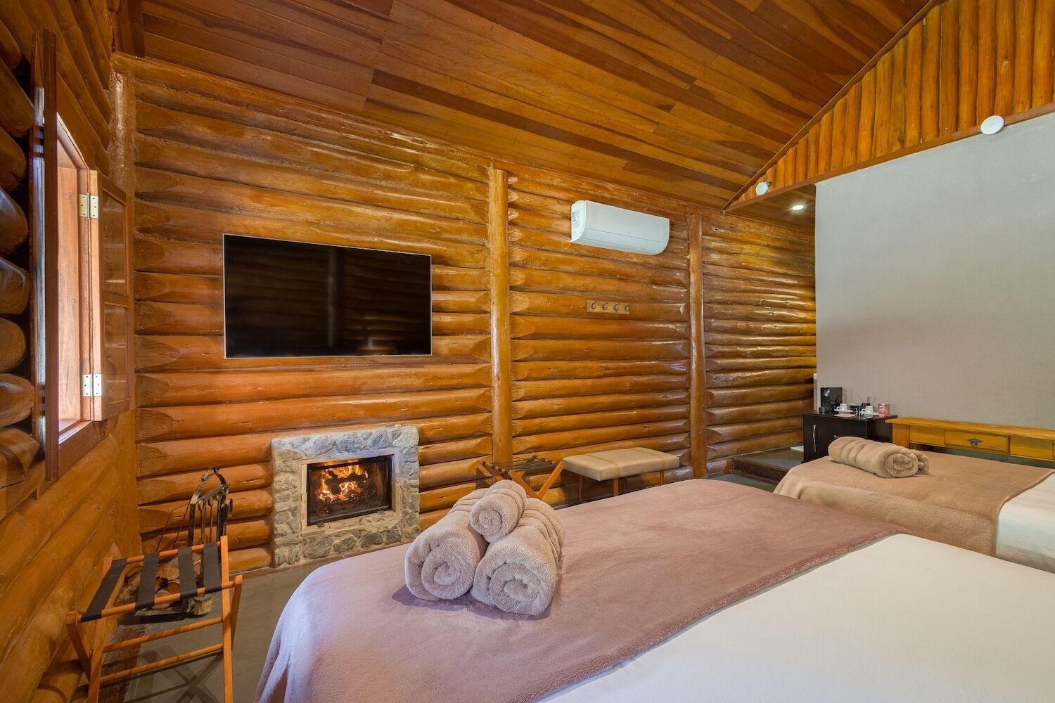 Una habitación tipo cabaña de madera con chimenea, televisión y dos camas.