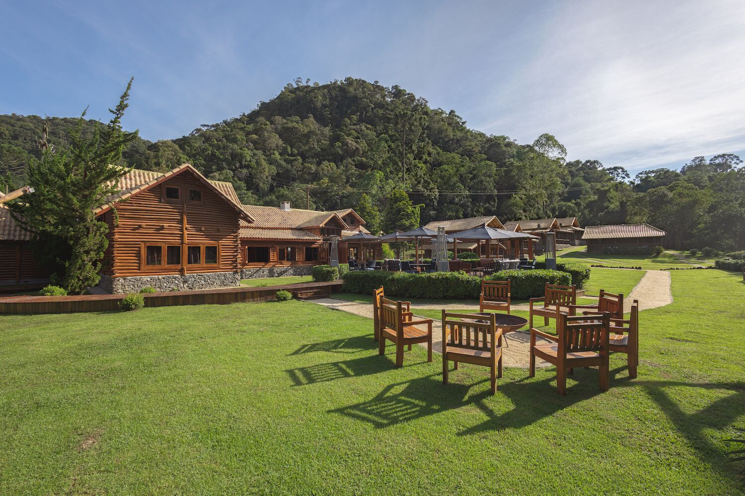 Un hotel de estilo cabaña de madera con asientos exteriores y vistas a una colina boscosa.
