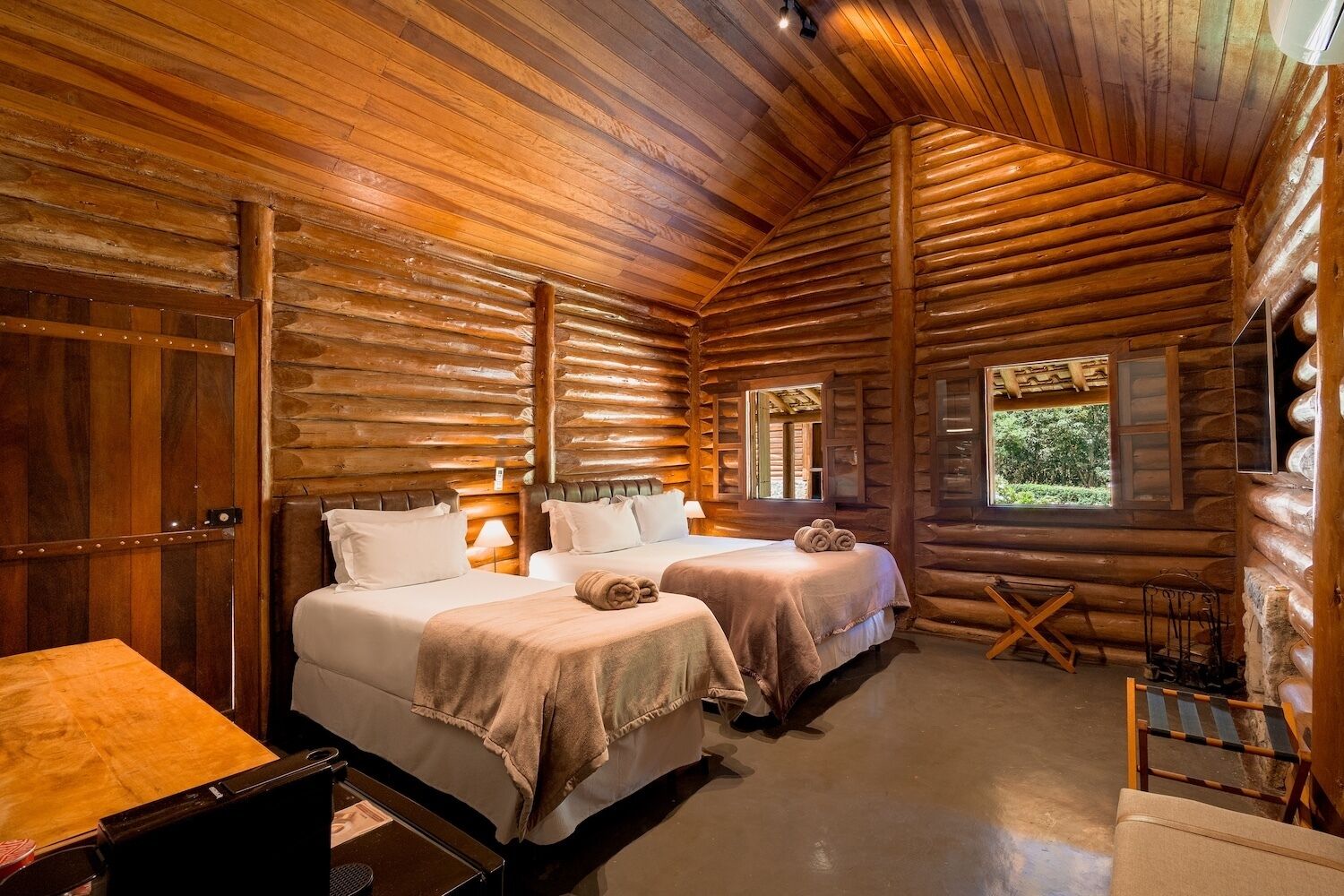 Habitación de cabaña de madera con dos camas, una mesa de madera y una ventana con vista a follaje.
