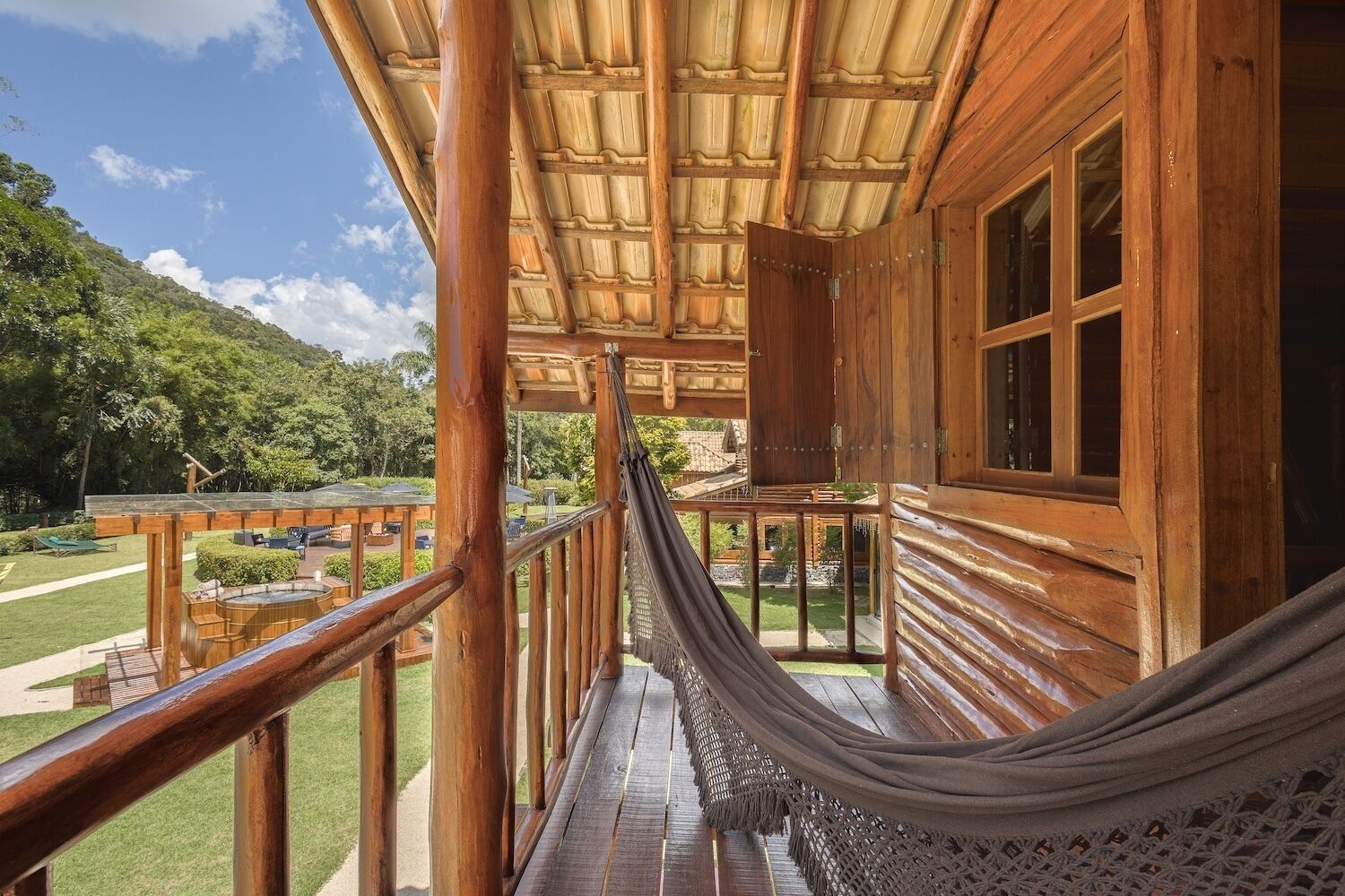 A wooden cabin with a hammock, wooden deck, and a view of a lush green landscape.