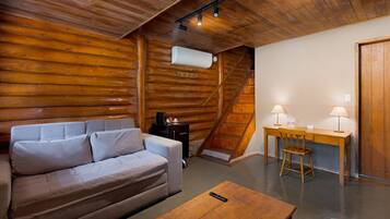 A log cabin interior with a sofa, a small table, a desk with two lamps, and a staircase.