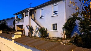 A two-story building with a white exterior, a balcony on the upper floor, and a stone staircase leading to the entrance.