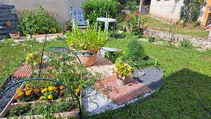 A garden with raised beds, a wooden deck, and a chair.