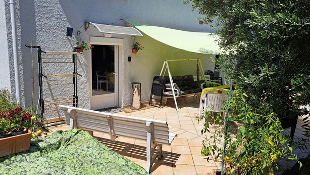 A patio with a bench, a table, and chairs. There are potted plants and a hanging chair.