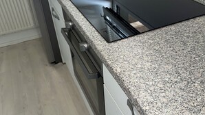 A kitchen with a granite countertop, a black induction cooktop, and stainless steel appliances. - one room apartment  (Hvidovre)