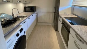 A compact kitchen with white cabinets, a built-in microwave, a stainless steel sink, a washing machine, and a refrigerator. - one room apartment  (Hvidovre)