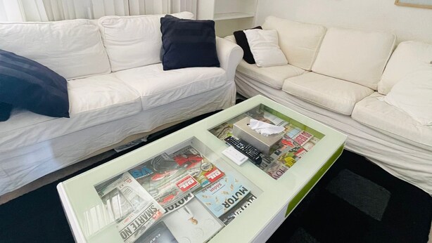 A living room with two white sofas, a glass coffee table with magazines, a bookshelf with books, and framed pictures on the wall. - one room apartment  (Hvidovre)