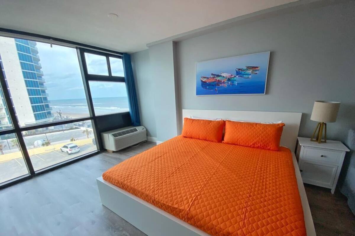A modern hotel room with a large bed, a view of the ocean, and a painting on the wall.