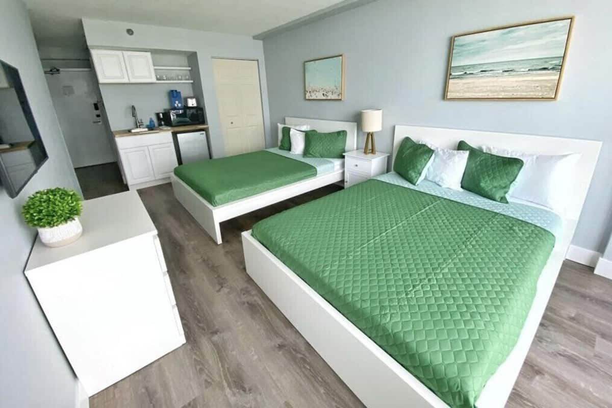 A bedroom with two beds, a kitchenette, and a bathroom.