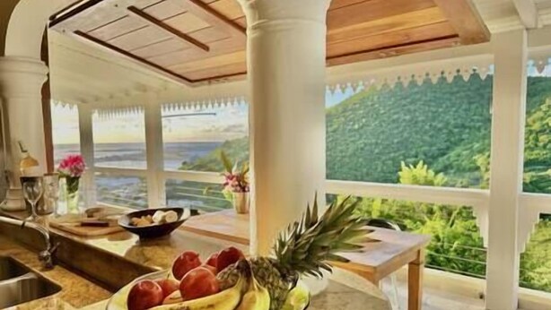 A dining area with a view of a bridge and greenery, featuring a fruit bowl on the counter. - Private 3bdr ocean view villa (Cole Bay)