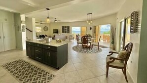 A spacious kitchen with a central island, a dining area with a round table, and a view of the outdoors. - Pelican Pearl Villa - GENERATOR (Sint Maarten)