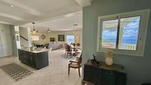A spacious living area with a kitchen, dining area, and a view of the ocean through a large window. - Pelican Pearl Villa - GENERATOR (Sint Maarten)