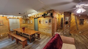 A cozy cabin interior with a wooden dining table, benches, a ceiling fan, and a fireplace sign.