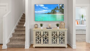 Una escalera que lleva a un rellano con un televisor sobre un mueble claro con objetos decorativos.