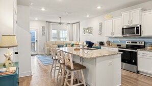 Una cocina moderna con armarios blancos, una isla central con taburetes de bar, electrodomésticos de acero inoxidable y vistas al salón.