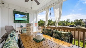 Un espacio de estar al aire libre techado, con una mesa de madera, sillas acolchadas y un televisor en la pared.