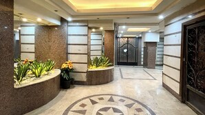 A lobby with a central circular mosaic floor design, recessed lighting, and potted plants along the walls.