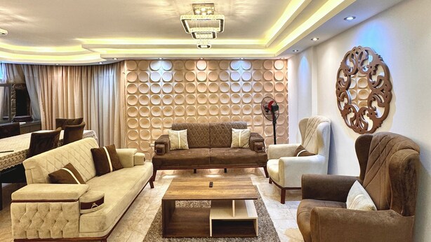 A modern living room with a sectional sofa, armchairs, a coffee table, and a decorative wall panel.