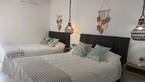 Ein Hotelzimmer mit zwei Betten, jeweils mit weißer Bettwäsche und gestreiften Kissen. An der Wand sind Lampen angebracht und auf dem Nachttisch steht eine kleine Pflanze.