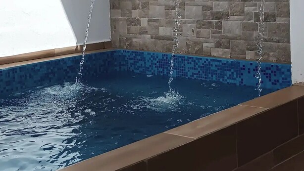 Ein Swimmingpool mit Wasserfällen von drei an der Wand befestigten Armaturen.