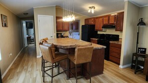 A modern kitchen with wooden cabinets, a central island with bar stools, and a pendant light fixture. - Bunk house on the ranch (Tyler)
