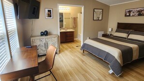 A bedroom with a bed, a desk, a chair, a ceiling fan, and a bathroom visible through an open door. - Bunk house on the ranch (Tyler)