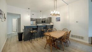 A modern kitchen with grey cabinets, a central island, and a dining area with wooden chairs and a table.