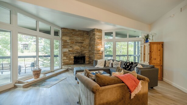 A spacious living room with a stone fireplace, large windows, and a cozy seating area.