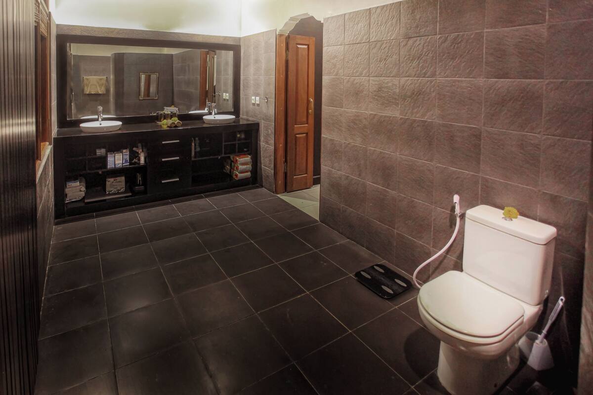 A modern bathroom with dark tiles, a white toilet, a sink with a mirror, and a wooden door.