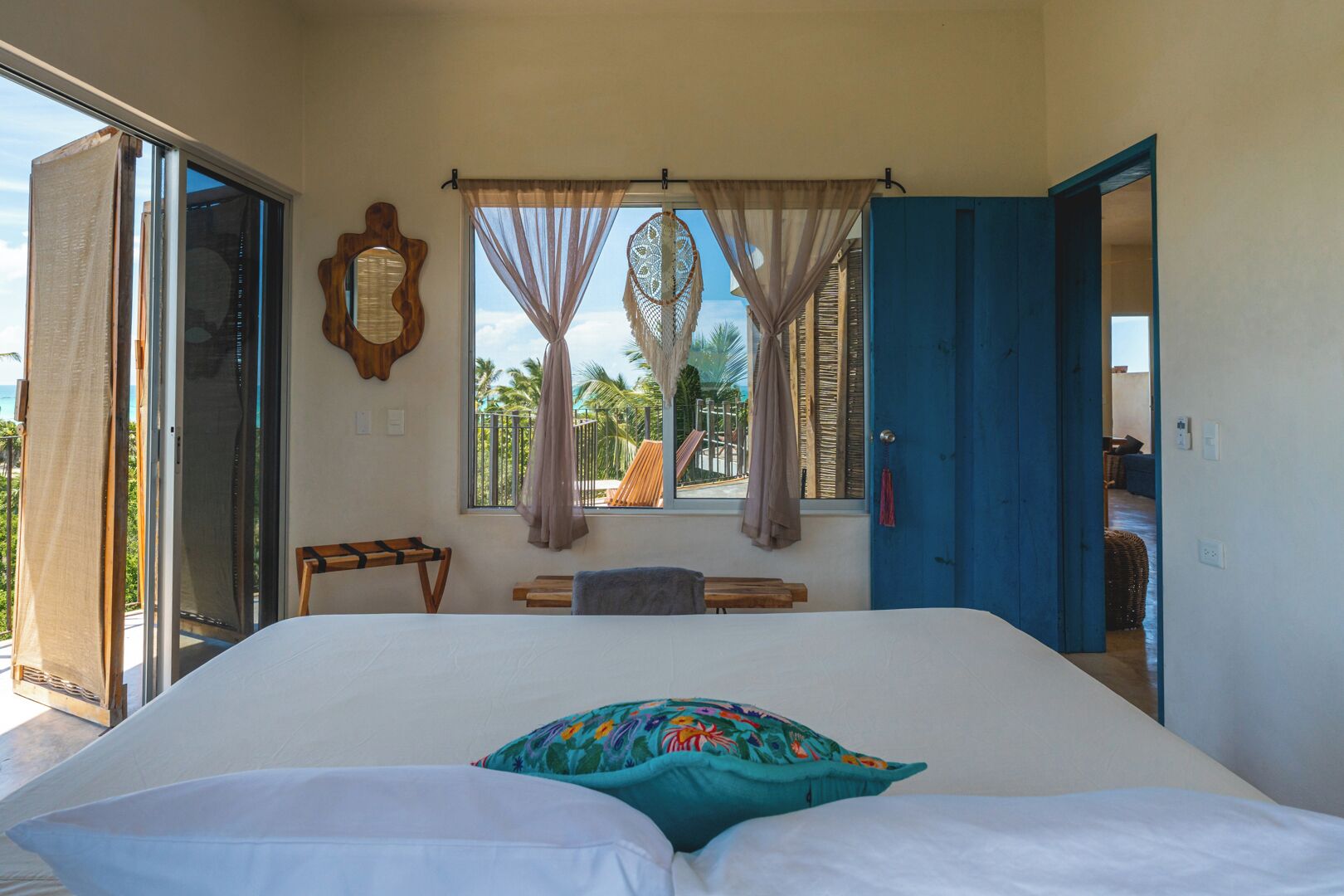 Un dormitorio con cama, una ventana con cortinas, una silla de madera y una puerta azul.
